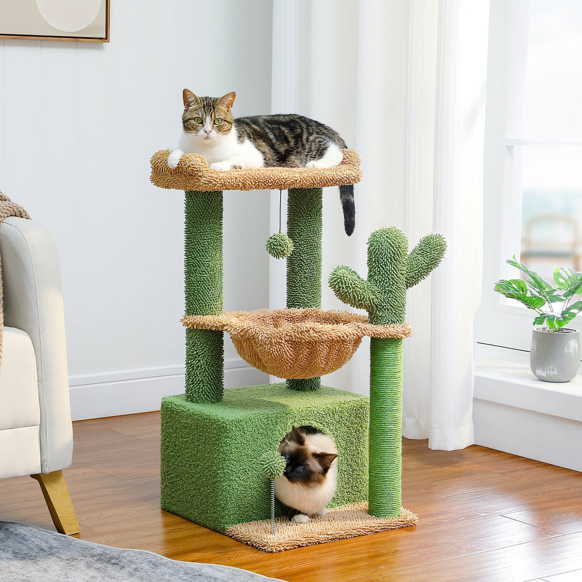 Grüner Kratzbaum in Kaktusform in einem hellen Wohnzimmer, auf dem eine Katze oben und eine weitere im unteren Häuschen sitzt