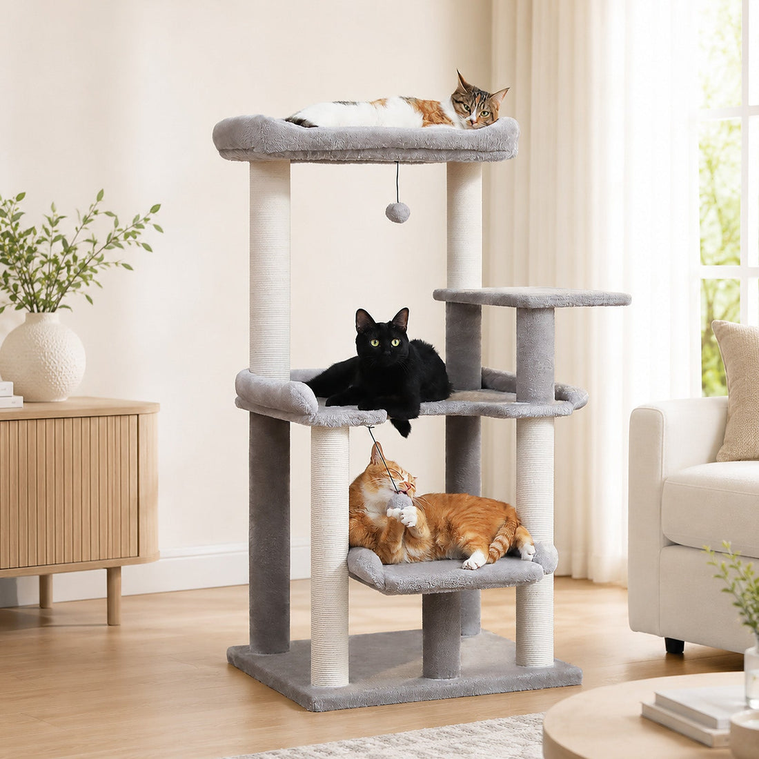 Drei Katzen auf verschiedenen Ebenen eines grauen Kratzbaums in einem hellen Wohnzimmer