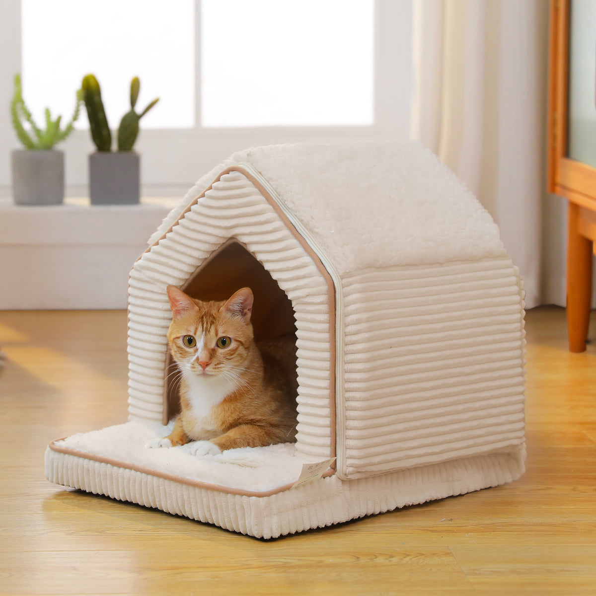 Orange tabby cat resting inside a house-shaped cream corduroy pet cave bed with a fluffy white sherpa roof