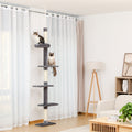 Slim charcoal grey floor-to-ceiling cat tower in a bright living room, tabby on the rimmed top perch and Siamese below