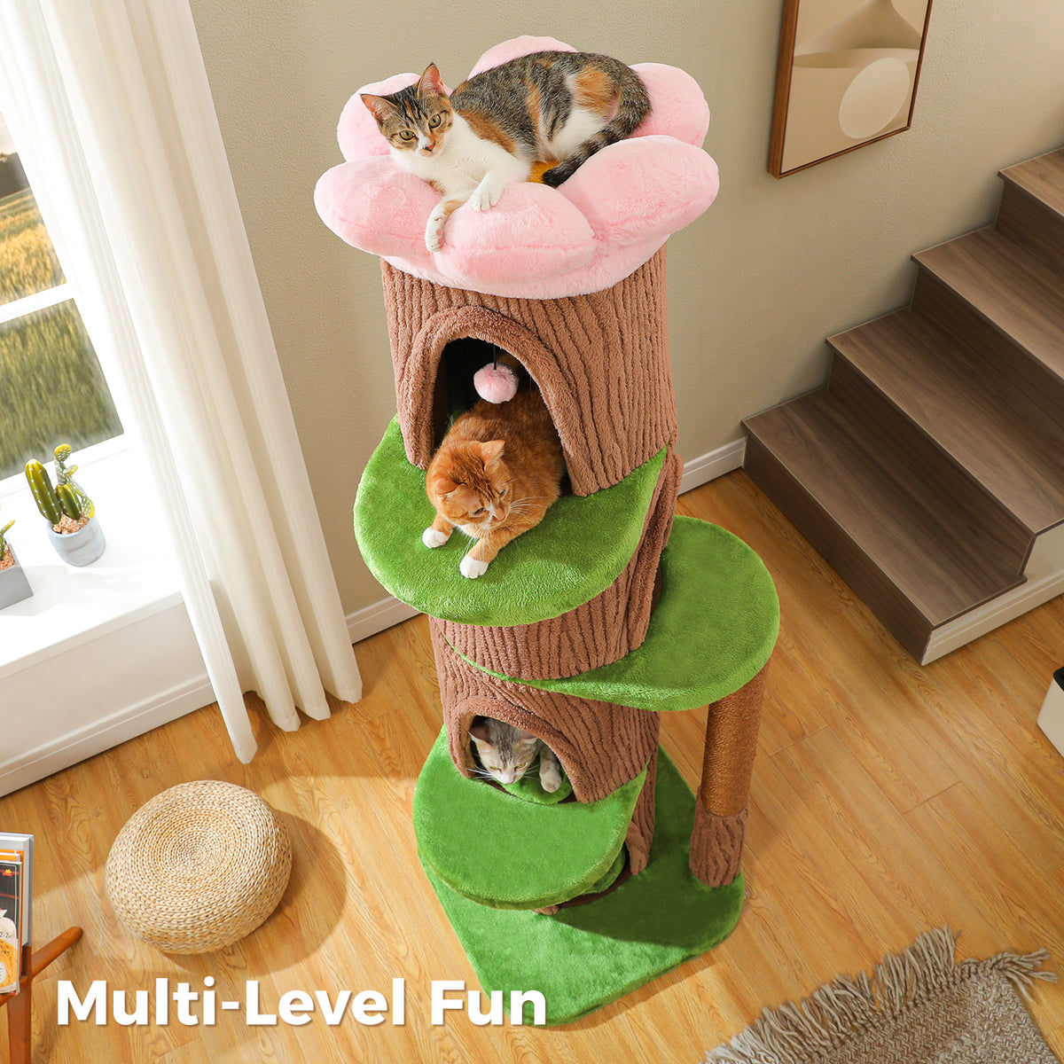Three-quarter view of the brown cat tree with green leaf platforms, calico in the pink flower bed and cats at the condos