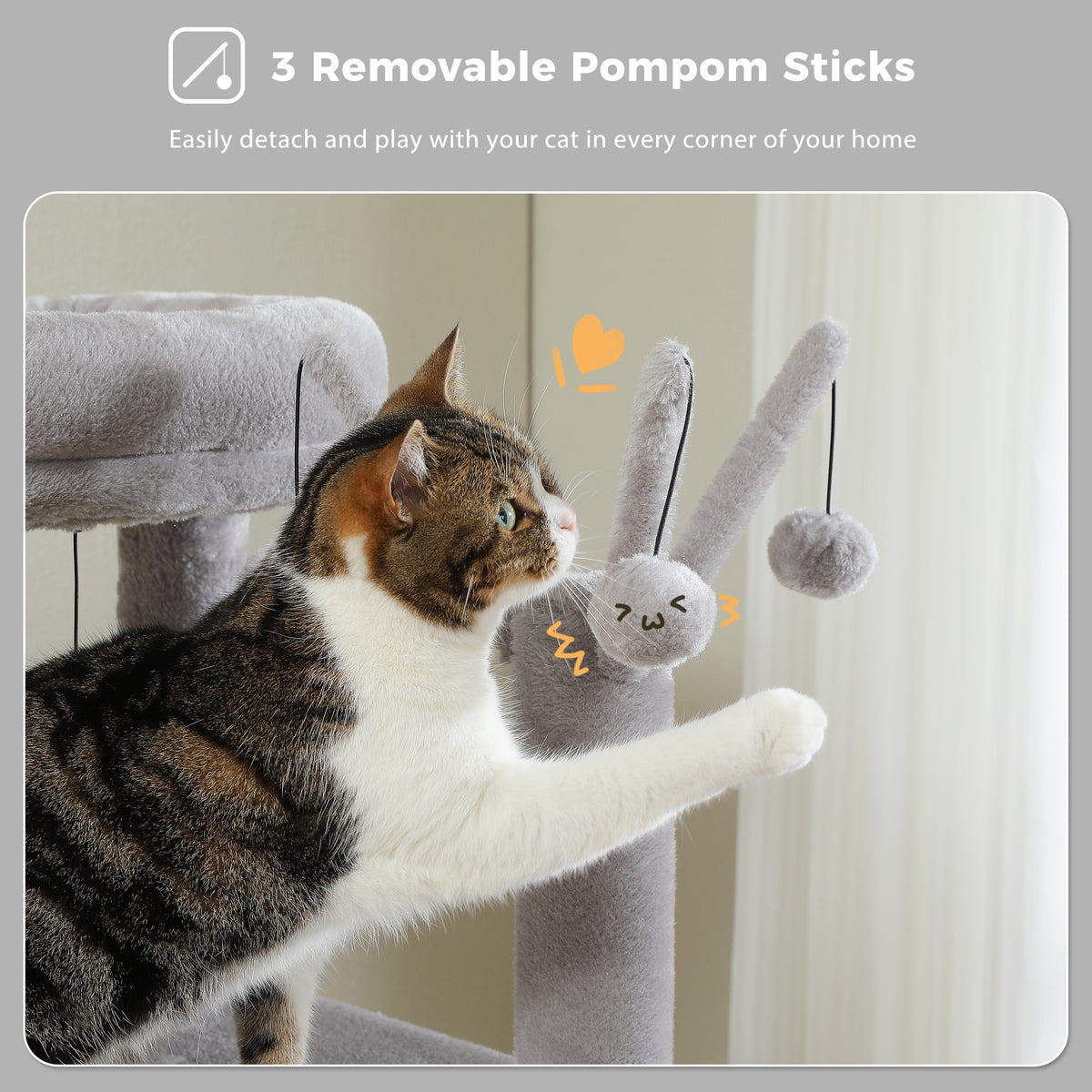 Calico tabby cat reaching up to bat a dangling grey pom-pom toy wand on the wide cat tree near a bright window