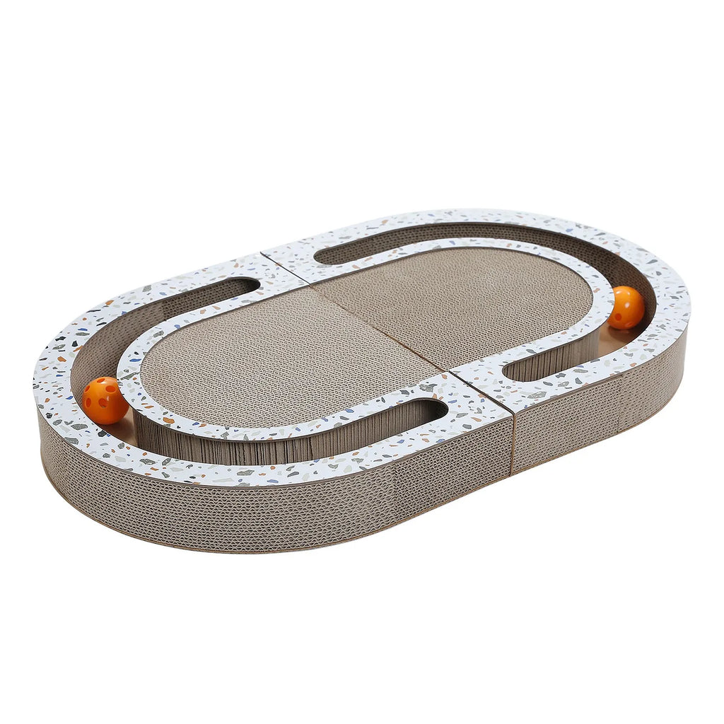 Oval corrugated cardboard cat scratcher with terrazzo-pattern trim and two orange balls in a track, studio shot