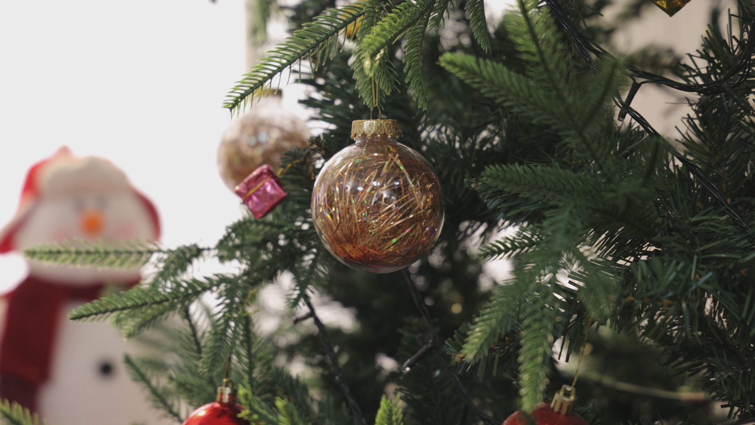 Video still opening on a Christmas tree: clear gold-tinsel bauble and red baubles with a snowman figurine